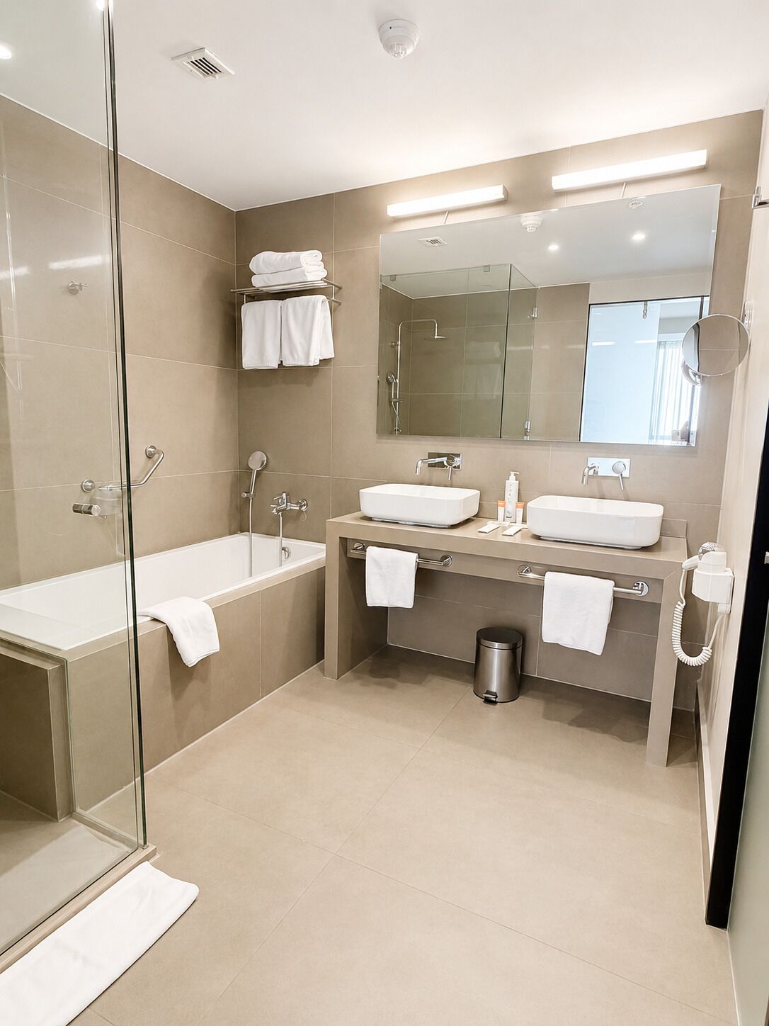 Un baño moderno con cabina de ducha de vidrio, tocador doble y un espejo grande.
