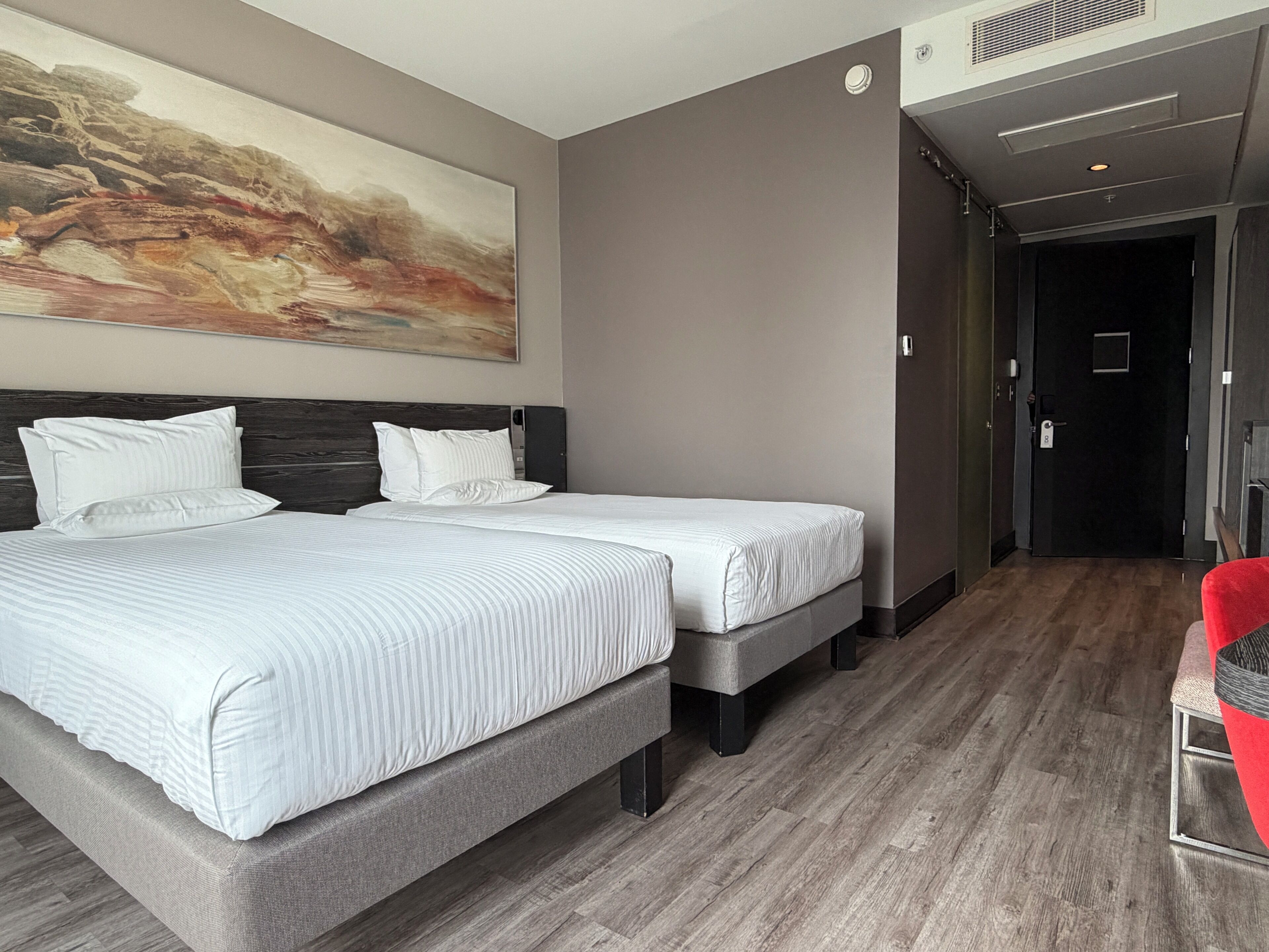 Habitación de hotel con dos camas, un cuadro abstracto grande en la pared y una silla roja.