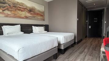 Habitación de hotel con dos camas, un cuadro abstracto grande en la pared y una silla roja.