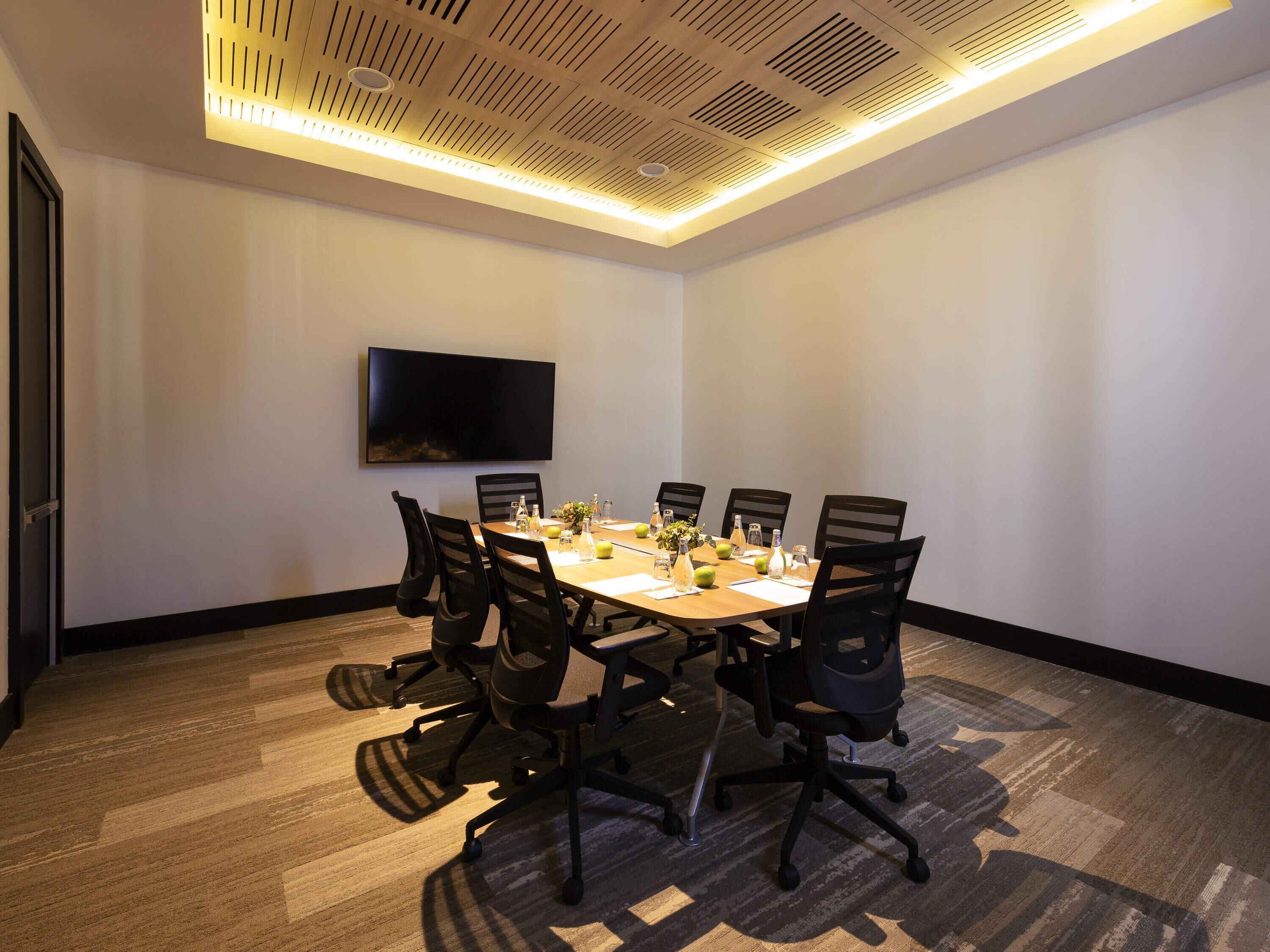 A conference room with a long table, chairs, a flat-screen TV, and a ceiling with ventilation.