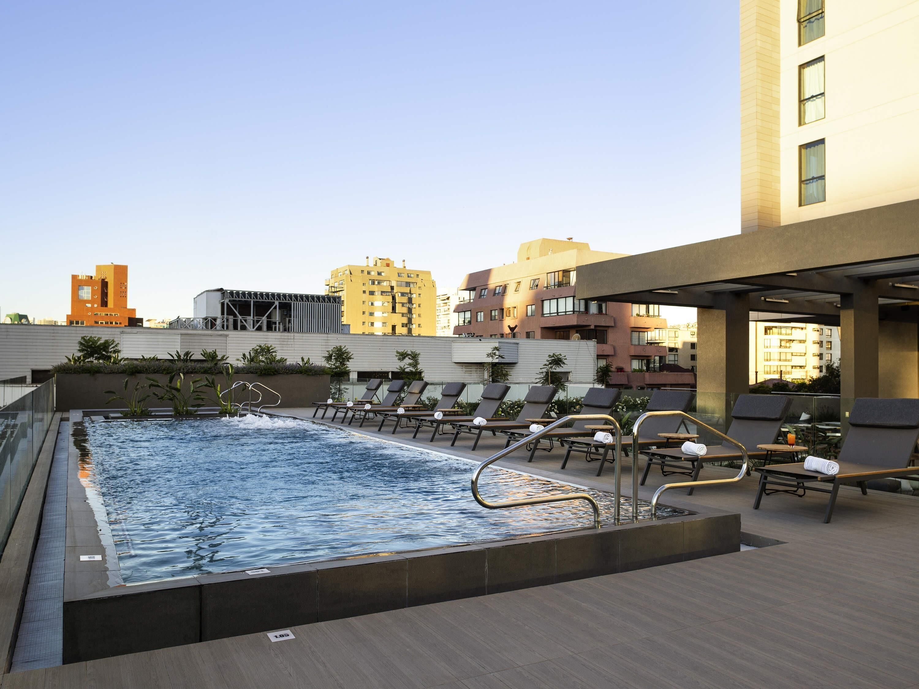 A rooftop pool with lounge chairs and a view of surrounding buildings.