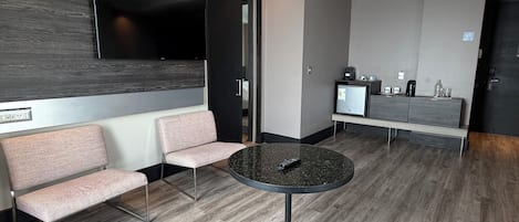 Un hall d’hôtel moderne avec une table ronde, un espace salon et un téléviseur à écran plat fixé au mur.