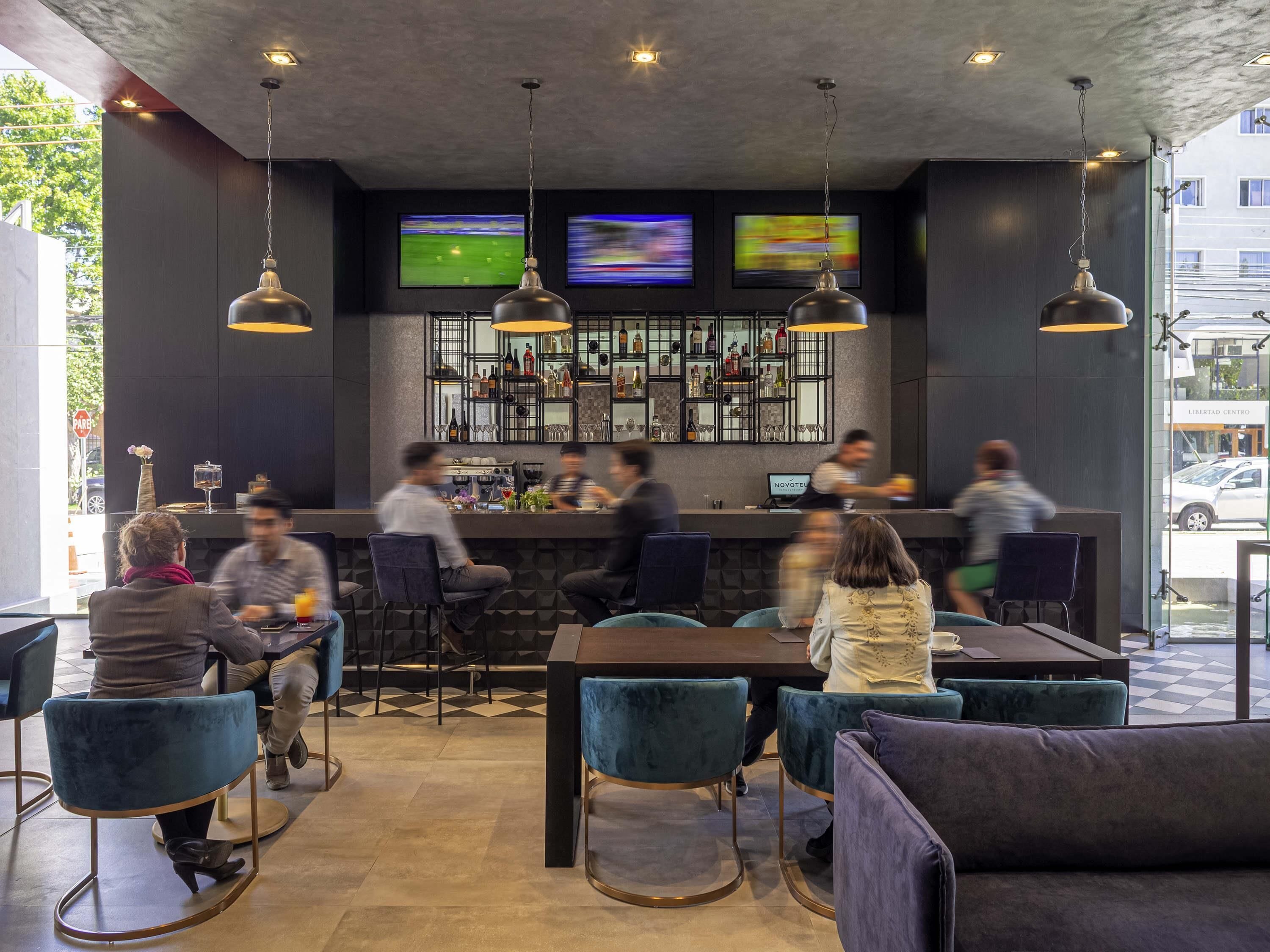 Zona de bar con varias pantallas, asientos y una barra.