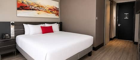 Une chambre d’hôtel moderne avec un grand lit, une table de chevet avec un téléphone, un tableau au mur et une porte sur le côté droit.