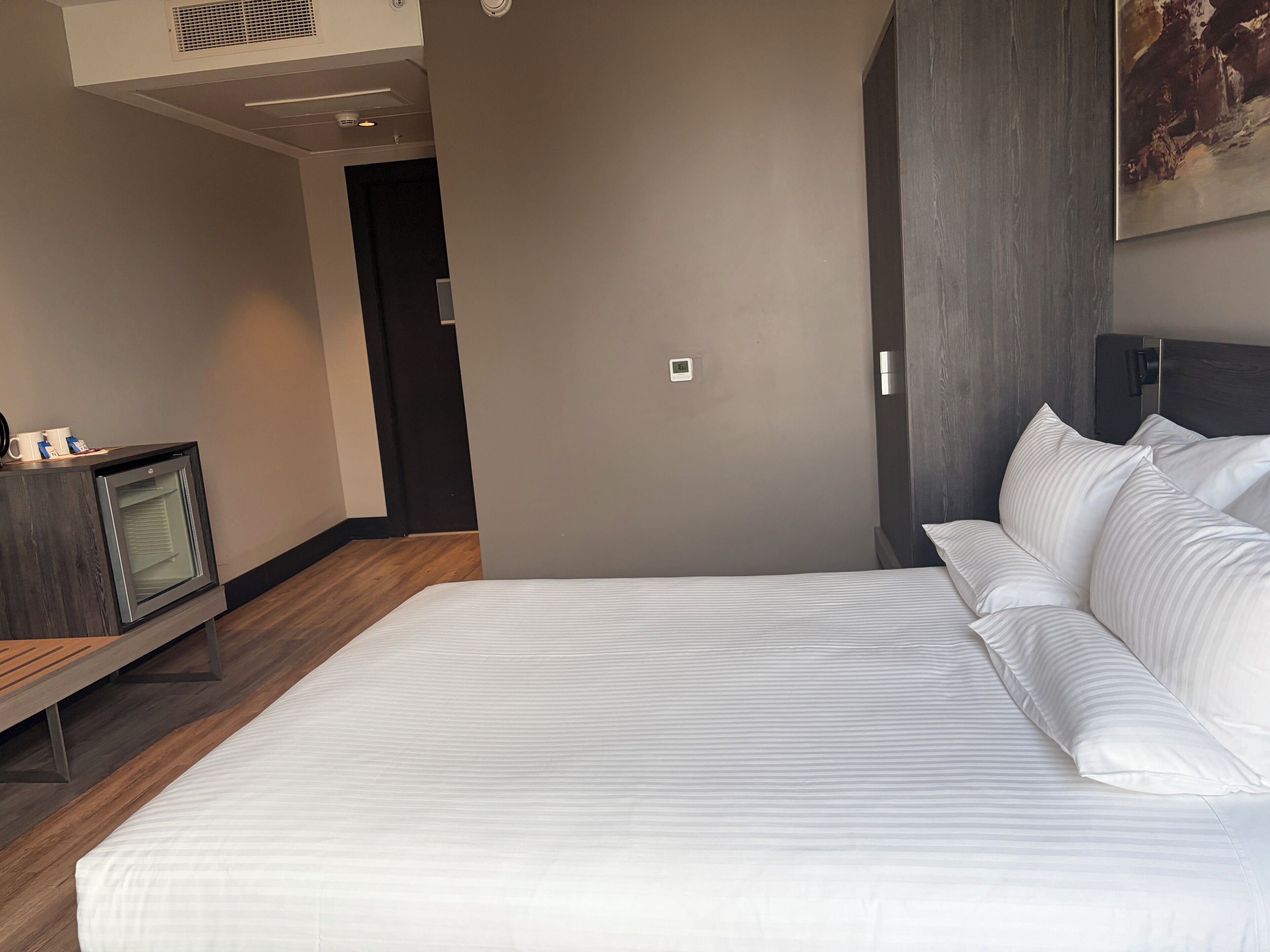 A modern hotel room with a large bed, a small television, and a painting on the wall.