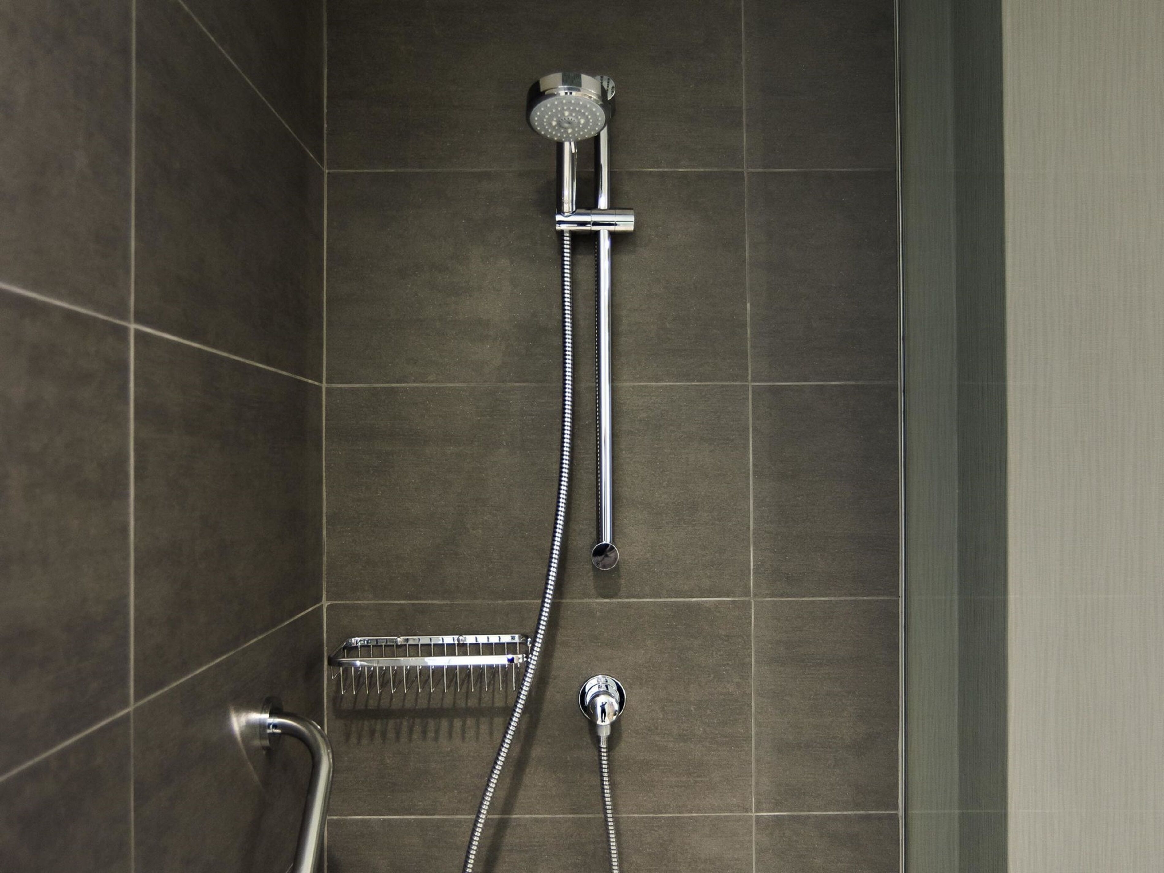A shower with a handheld showerhead and a wall-mounted faucet.