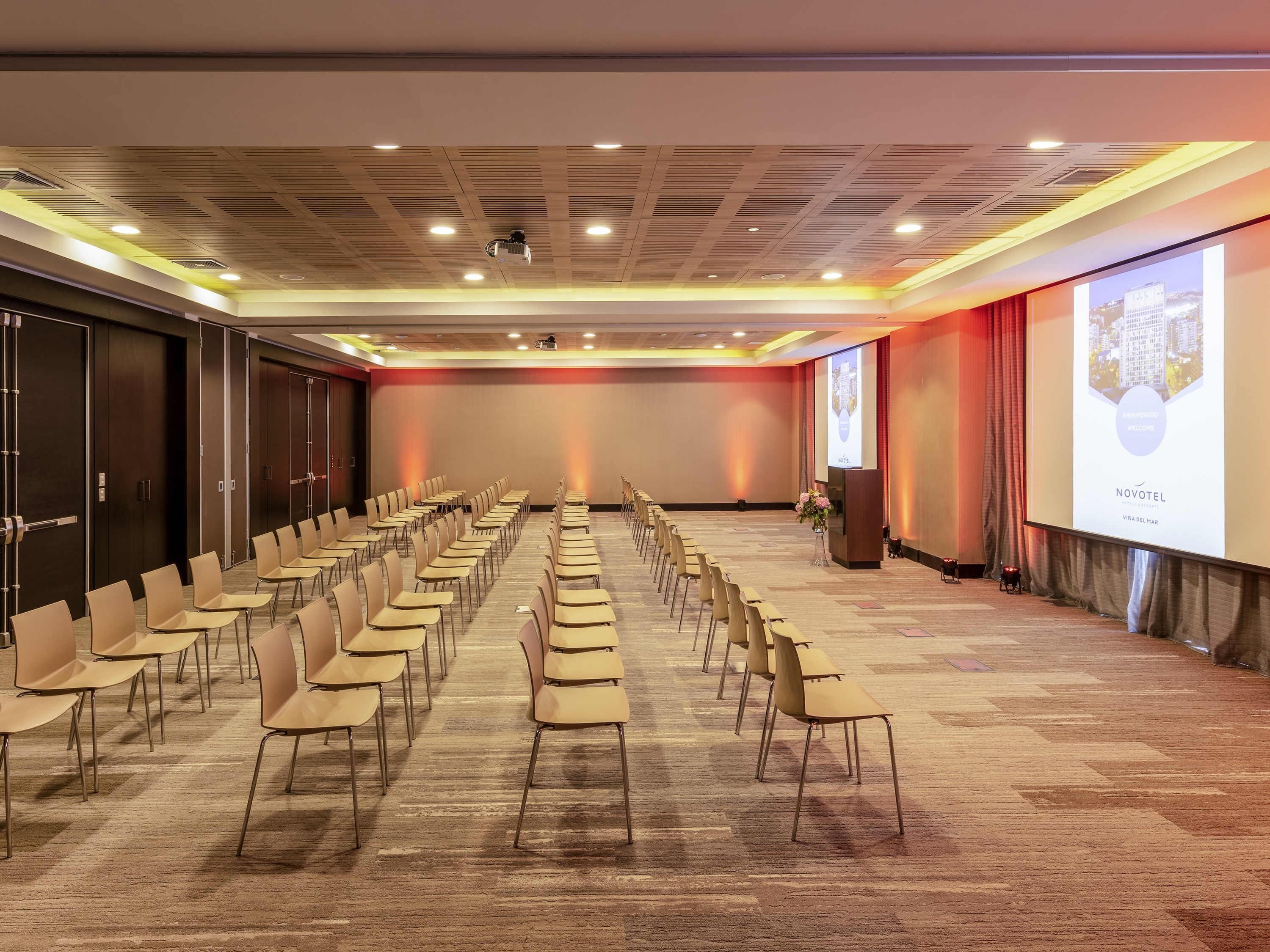 Un salón de conferencias con filas de sillas, una pantalla para proyector y un atril.