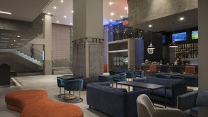 Een moderne hotellobby met een trap, zithoeken en een bar.