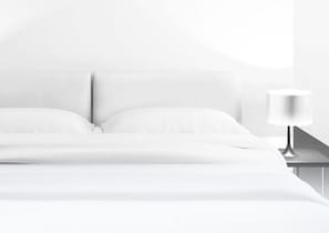 A bed with white linens, a nightstand with a lamp, and a plain wall. - Ibis Styles Douai Gare Gayant Expo (DOUAI)