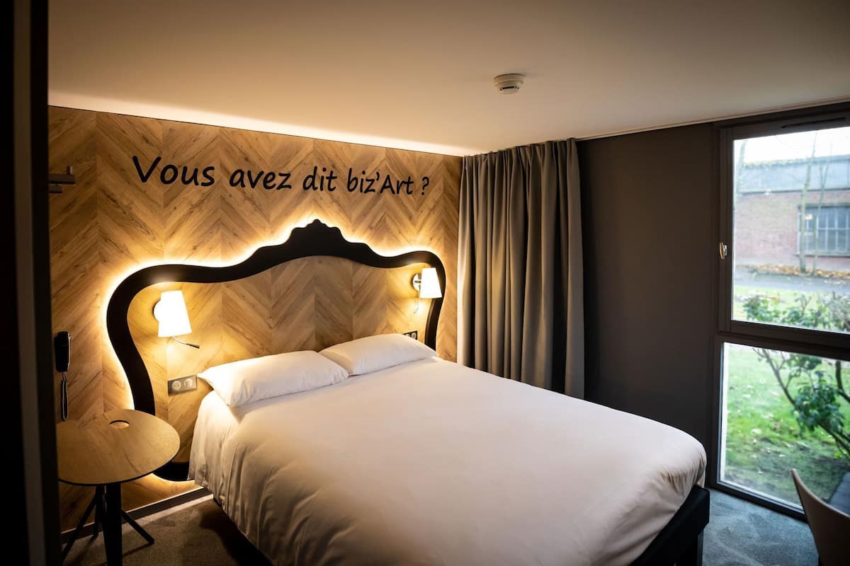 A hotel room with a bed, bedside lamps, a desk, and a window with a view.