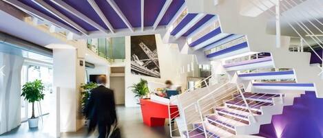 A modern interior with a central staircase, a reception desk, and a large window.