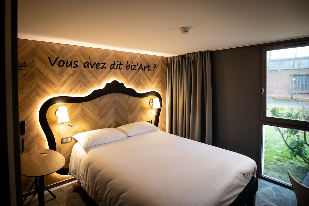 A hotel room with a bed, bedside lamps, a desk, and a window with a view.