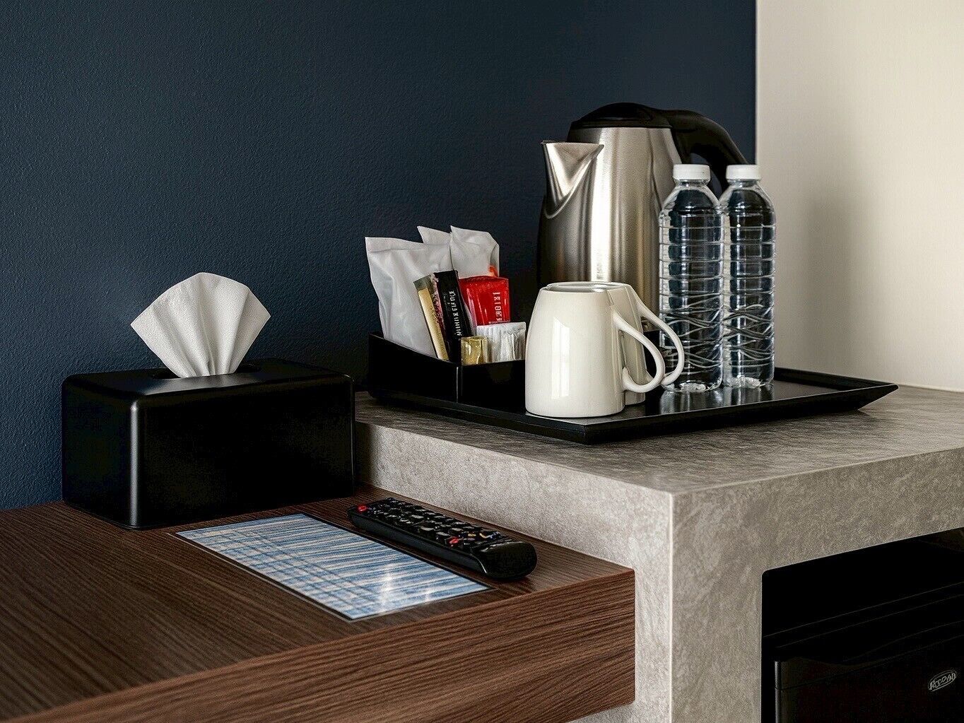 Ein Hotelzimmer-Schalter mit Taschentuchbox, Fernbedienung, Tablett mit Tasse, Wasserkocher und Wasserflaschen.