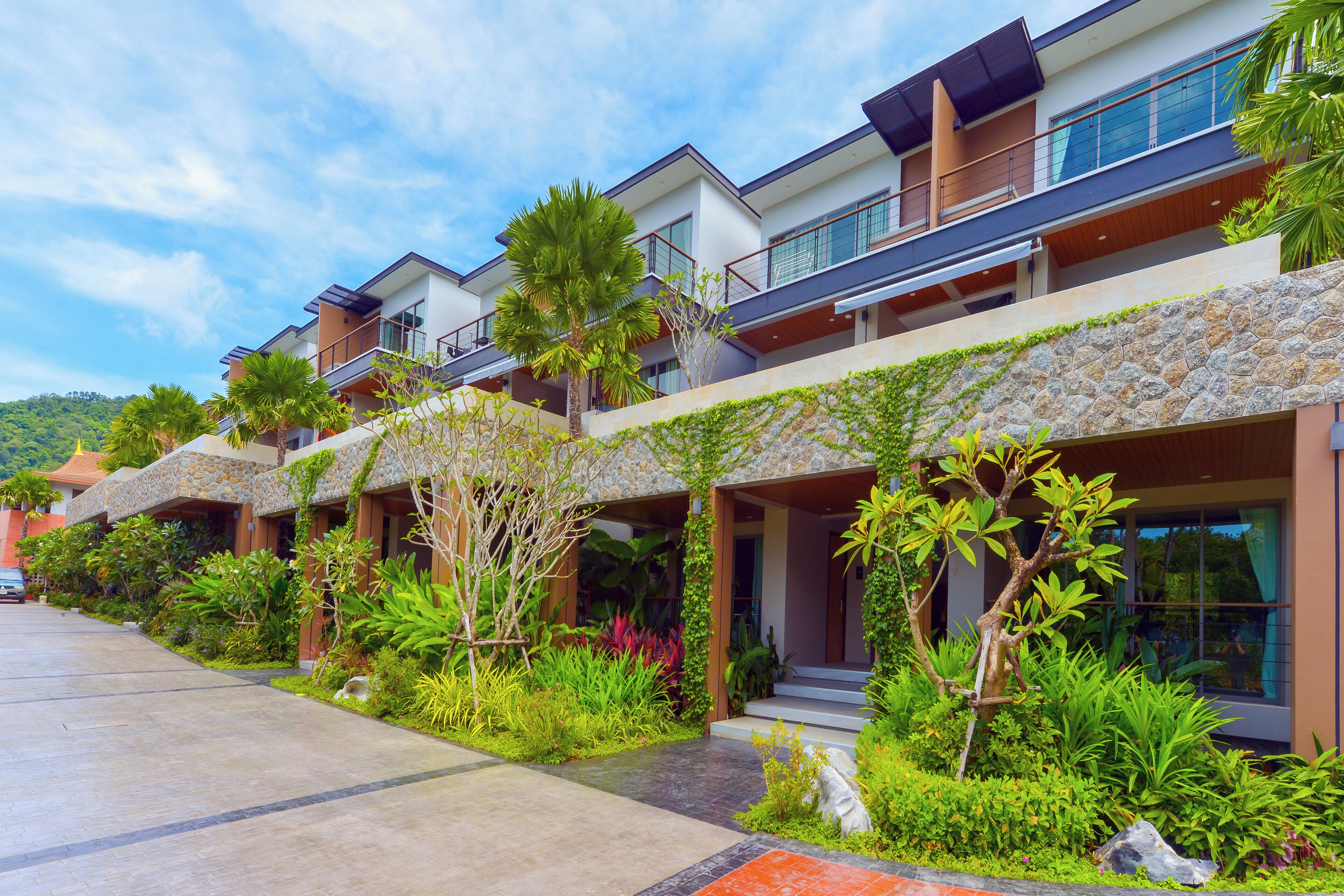 A modern hotel with multiple balconies, lush greenery, and a stone facade.