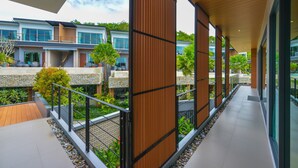 A modern hotel corridor with wooden paneling, glass doors, and a view of other hotel buildings. - Le Resort and Villas (Rawai)