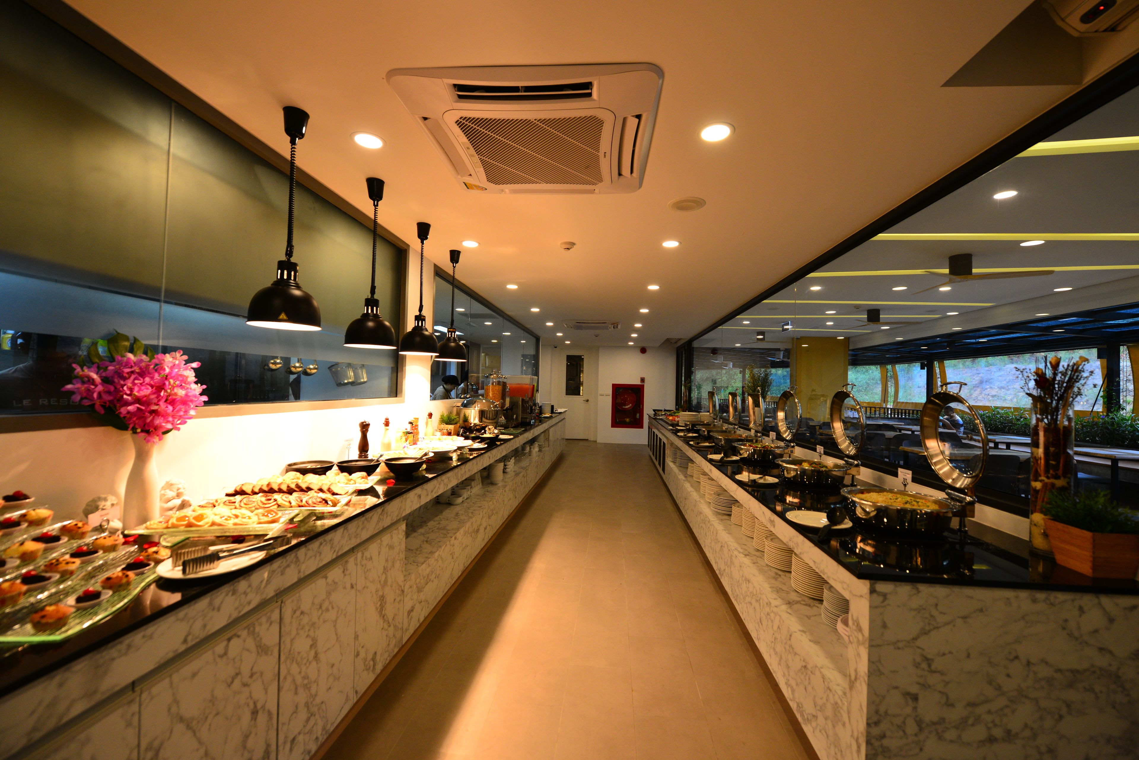 A modern hotel buffet with marble countertops, overhead lighting, and a view of the outdoors.