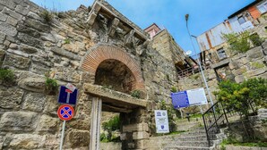 Ein uraltes Steinhaus mit einem großen Bogenportal, einer nach oben führenden Treppe und einem Schild, das den UNESCO-Status kennzeichnet.