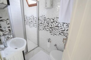 Un baño con lavamanos, inodoro y zona de ducha blanca.