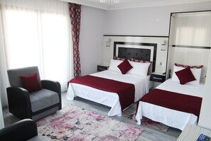 A hotel room with two beds, a chair, a nightstand, and a large window with curtains. - Kural Pansiyon (Amasra)