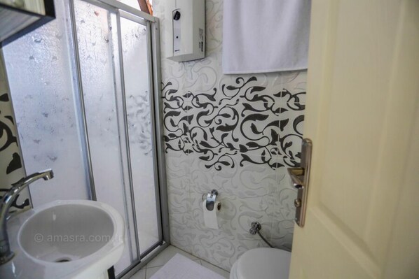 A bathroom with a glass shower door, a sink, and a toilet. - Kural Pansiyon (Amasra)