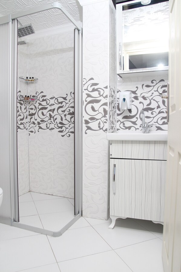 A bathroom with a shower, a toilet, and a sink with a mirror. - Kural Pansiyon (Amasra)
