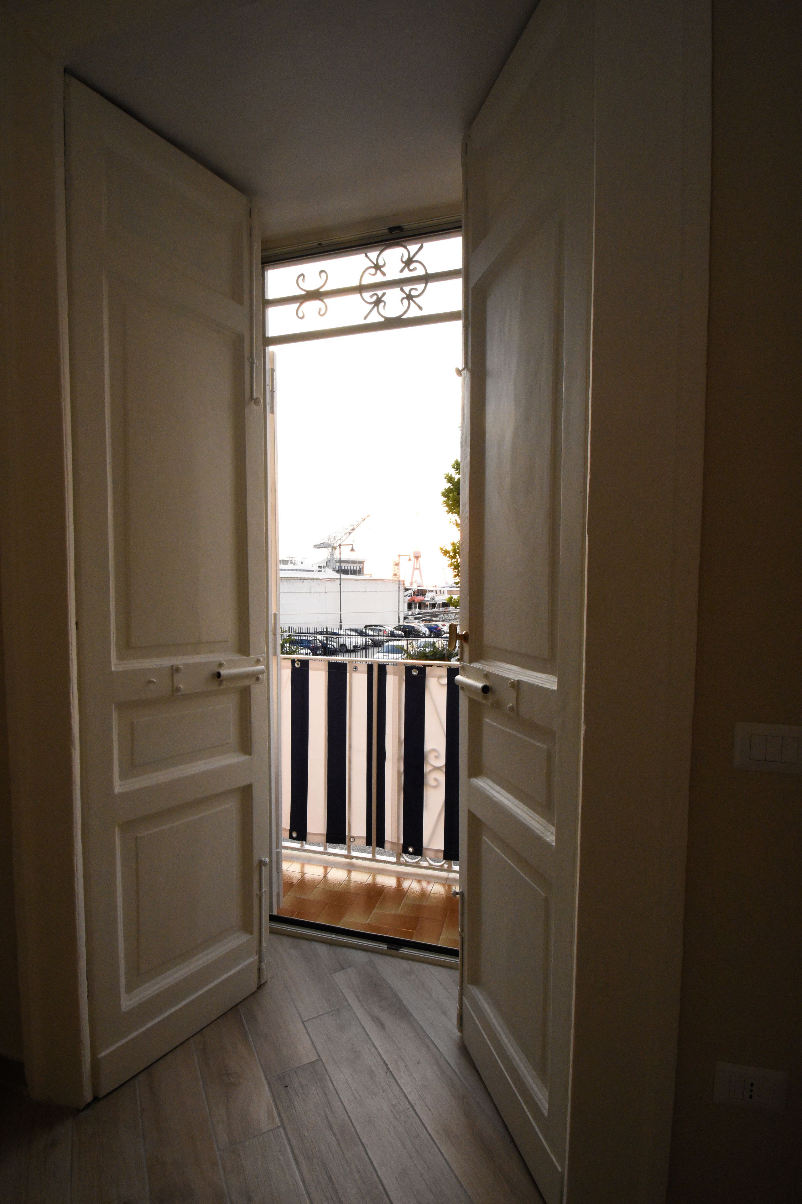 A hallway with a door leading to a balcony with a metal railing.
