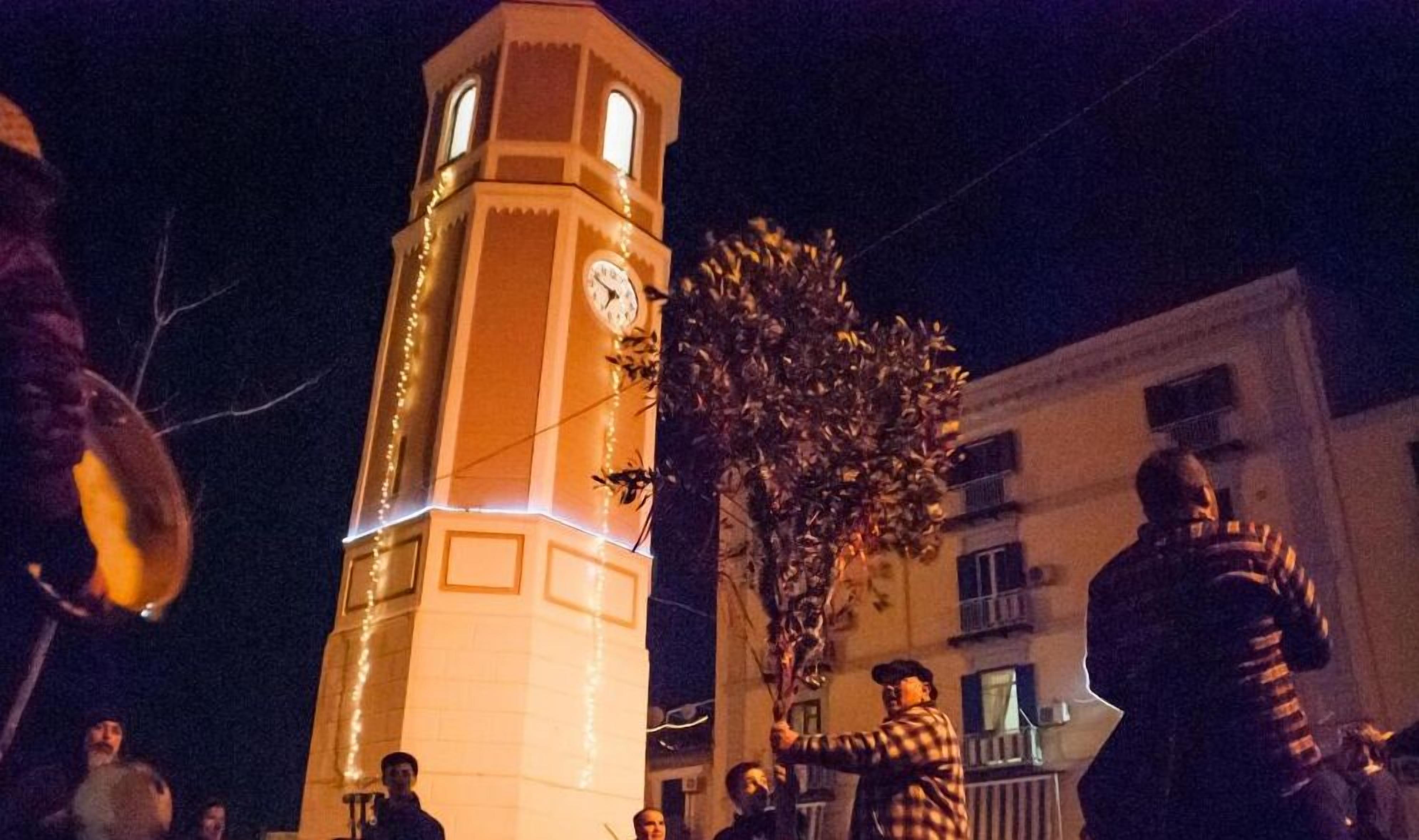 A clock tower with a clock face, surrounded by buildings and people.