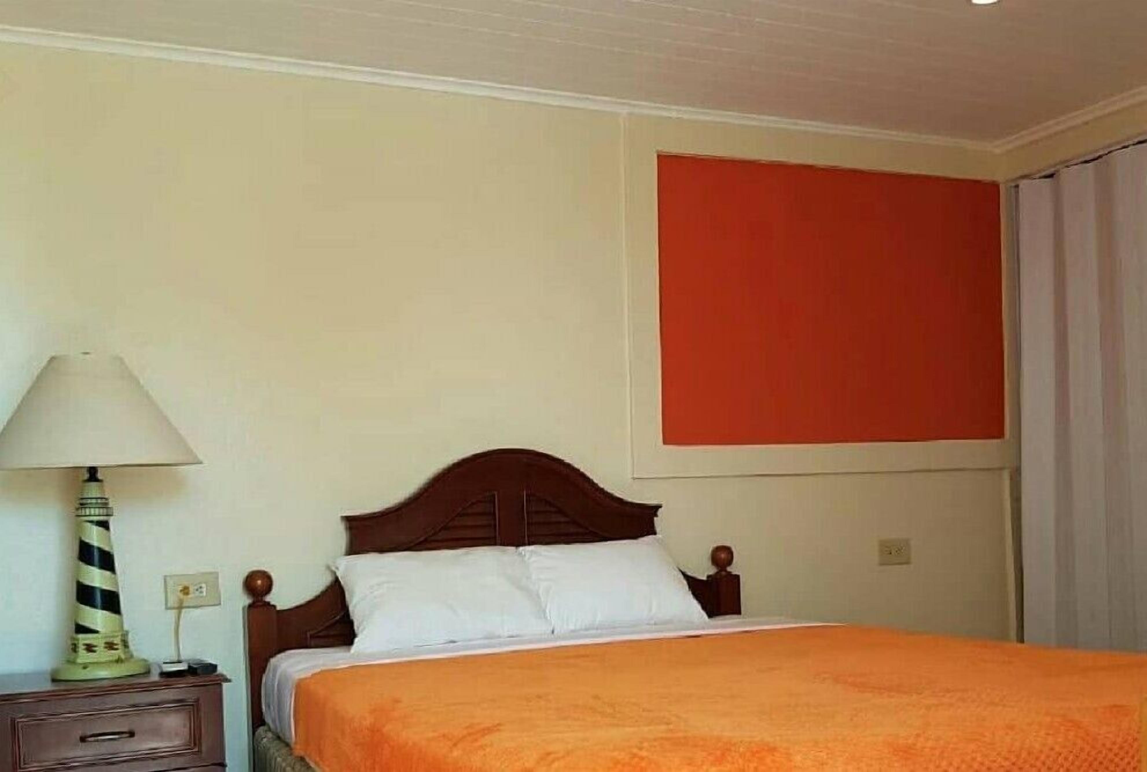 A hotel room with a bed, a nightstand with a lamp, and a red accent wall.