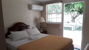Ein Hotelzimmer mit Bett, Klimaanlage, Fenster mit Jalousien und Blick ins Freie.