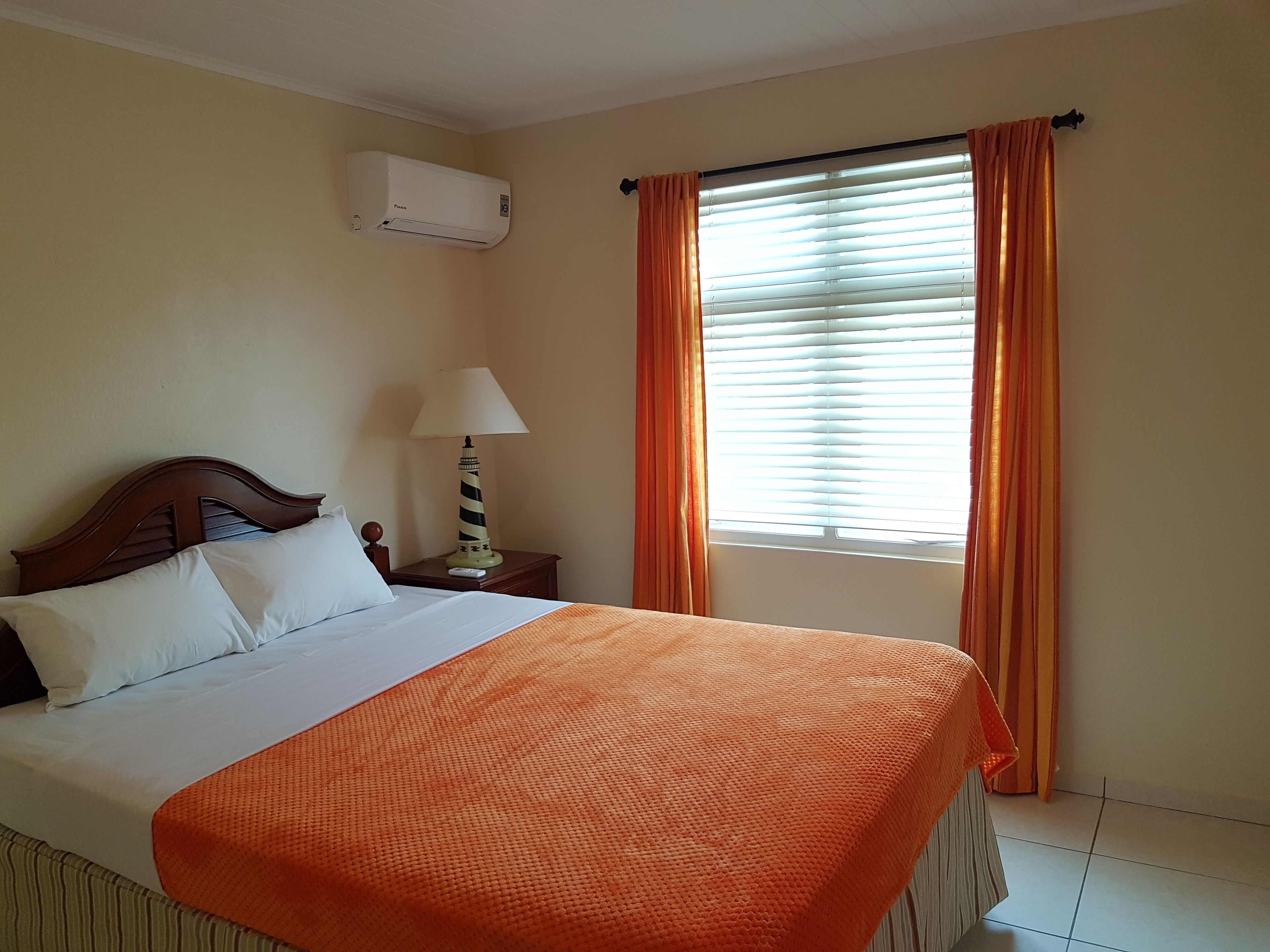 Une chambre d’hôtel avec un lit, un climatiseur, une table de chevet avec une lampe et une fenêtre avec des rideaux.