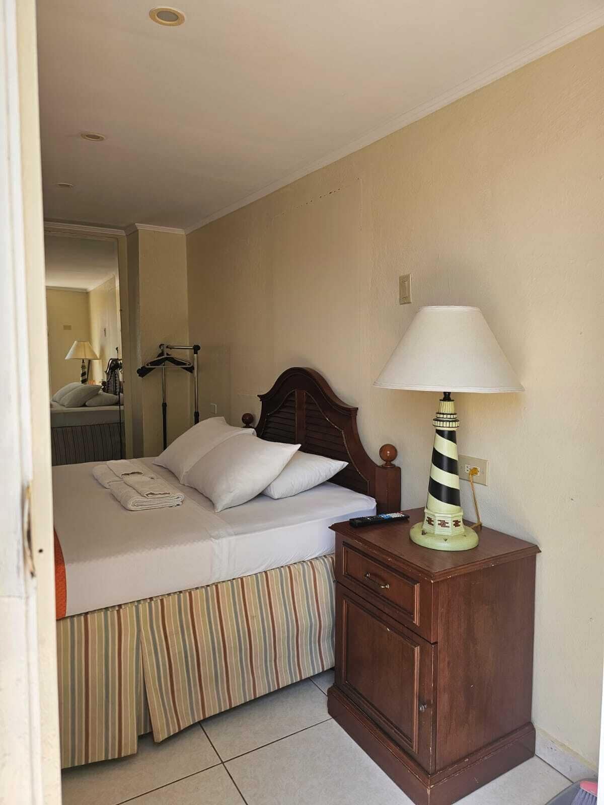 Et hotelværelse med en seng, et trænatbord, en lampe og et sengetæppe med striber.