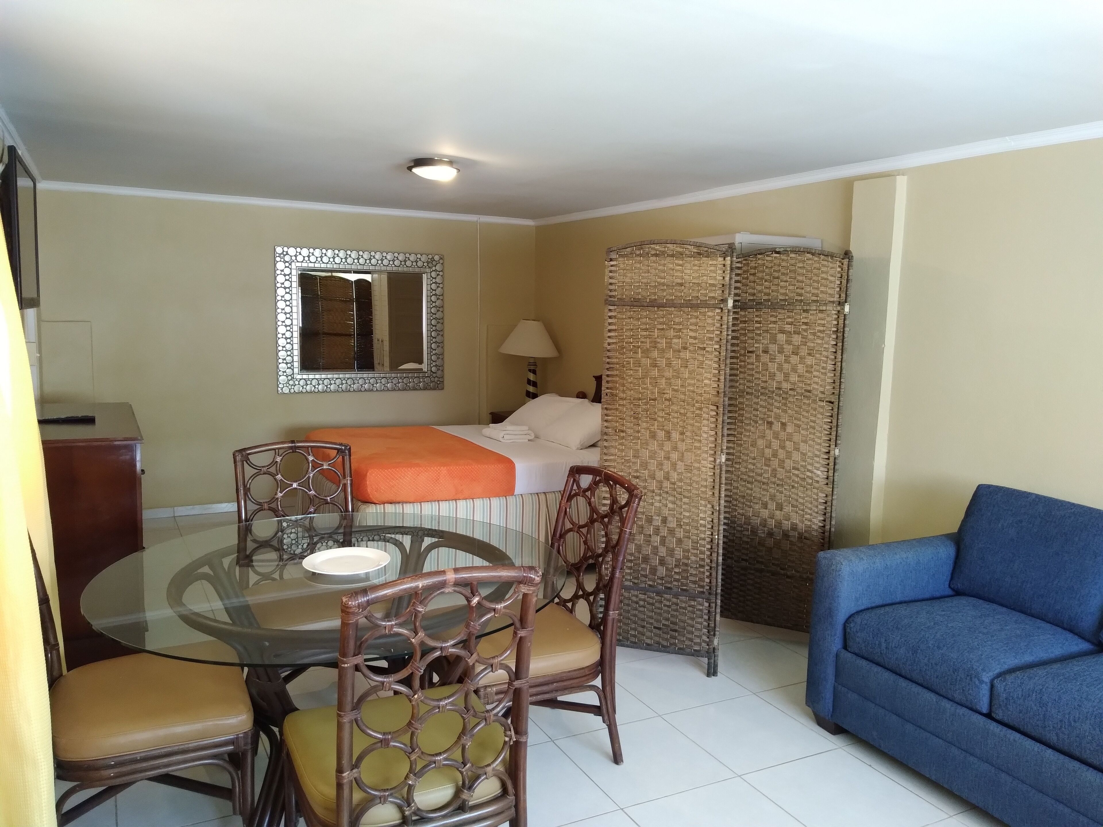Una habitación de hotel compacta con cama, una mesa de comedor con sillas, un sofá azul y un espejo decorativo.