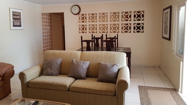 Ein Wohnzimmer mit einem gestreiften Sofa, einem Esstisch mit Stühlen, einer Wanduhr und einem dekorativen Wandpaneel.
