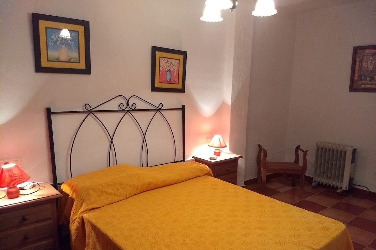 A bedroom with a bed, two bedside tables with lamps, a chair, and a radiator.