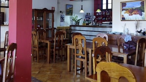Un comedor con sillas y mesas de madera, un pilar rojo y una zona de cocina al fondo.