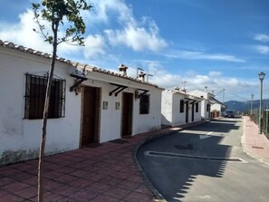 A narrow street lined with white buildings, each with a single door and window, under a clear sky. - Apartamentos Mirador de Jubrique (Jubrique)