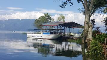 A boat docked at a pier with a covered seating area and a sign for Lake Yojoa Cruises.