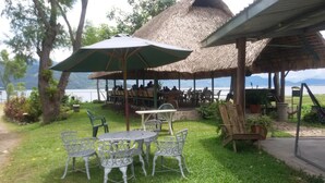 An outdoor seating area with tables and chairs, a thatched-roof structure, and a view of a body of water. - Honduyate (Santa Cruz de Yojoa)