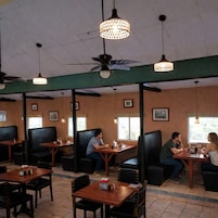 Un restaurante con cabinas, mesas, ventiladores de techo e iluminación colgante.