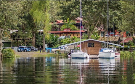 A tranquil marina with boats docked, surrounded by lush greenery and buildings with red roofs.