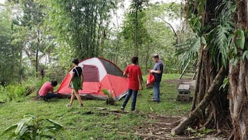 A group of people around a red and white tent in a forested area.