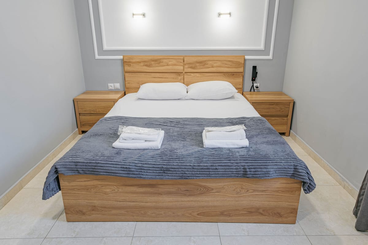 A neatly made bed with a wooden headboard, two bedside tables, and a wall-mounted light fixture.
