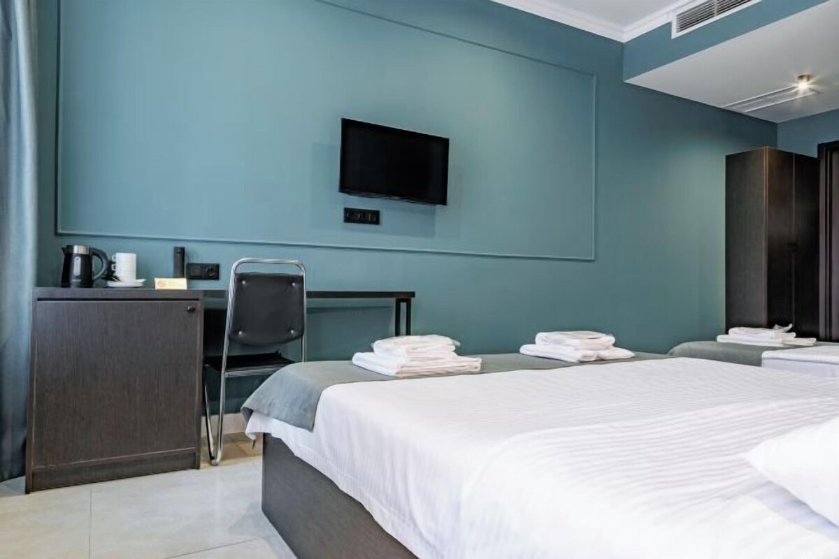 A modern hotel room with a large bed, a desk, a chair, and a flat-screen TV mounted on the wall.