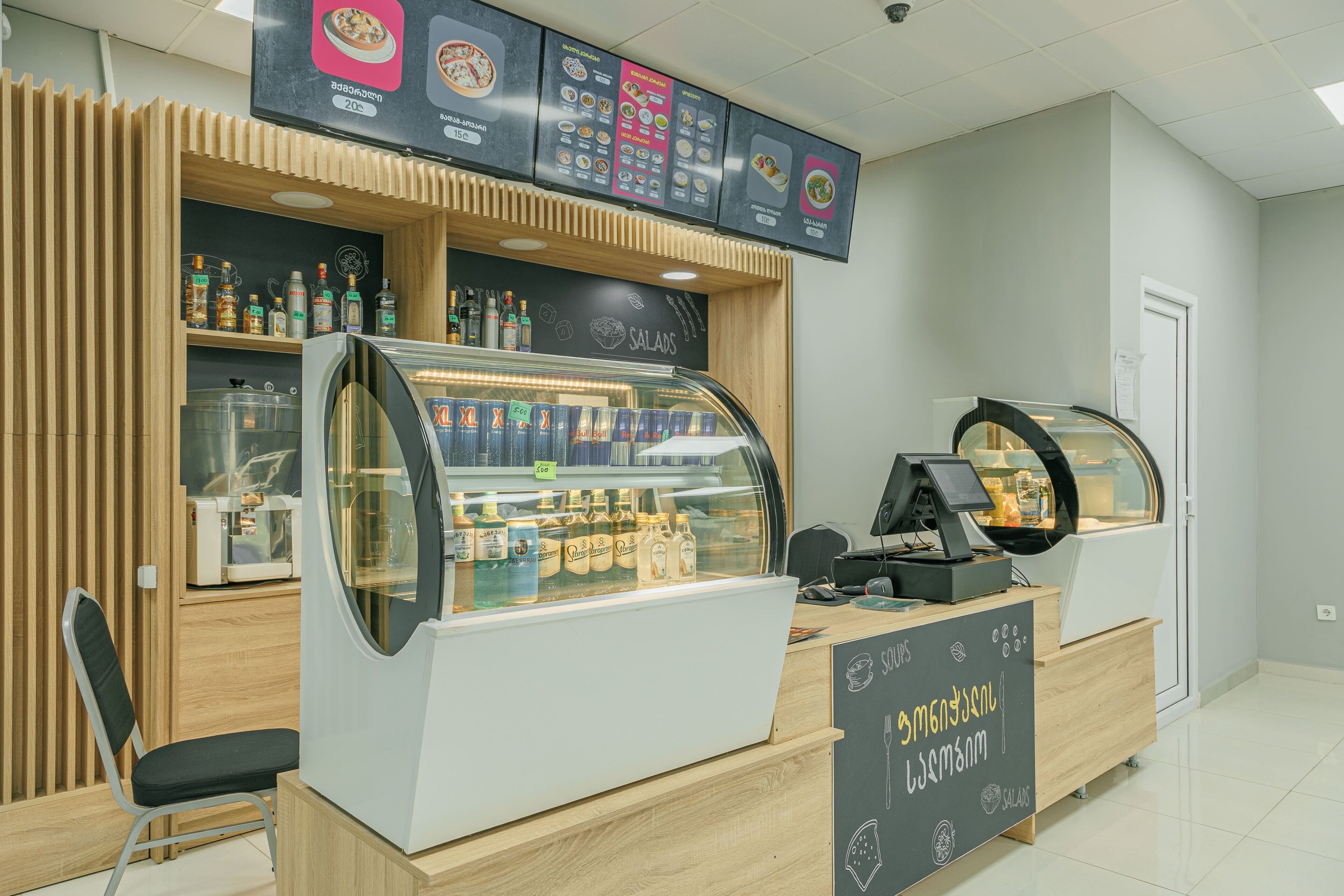 A food counter with a menu board above, a refrigerated display case, and a wooden counter.