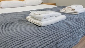 A neatly made bed with a grey textured blanket, white pillows, and folded white towels on the side. - Route Hotel (Tbilisi)