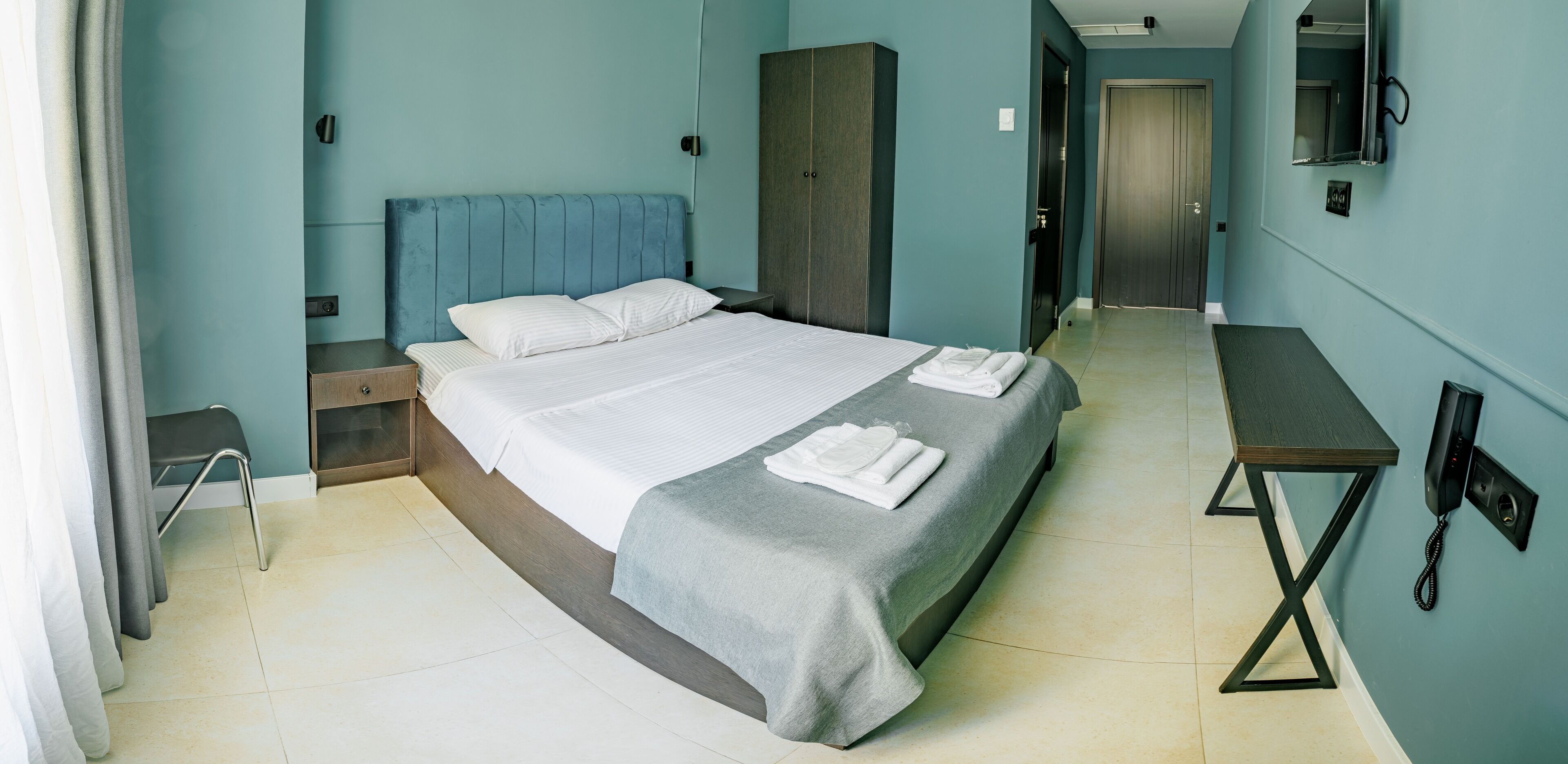 A hotel room with a bed, a bedside table, a wardrobe, a desk, and a telephone.