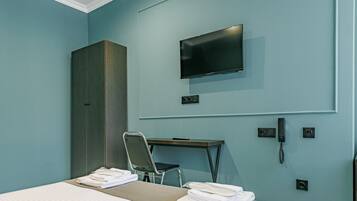 A hotel room with a bed, a desk, a chair, a wardrobe, a flat-screen TV, and a telephone.