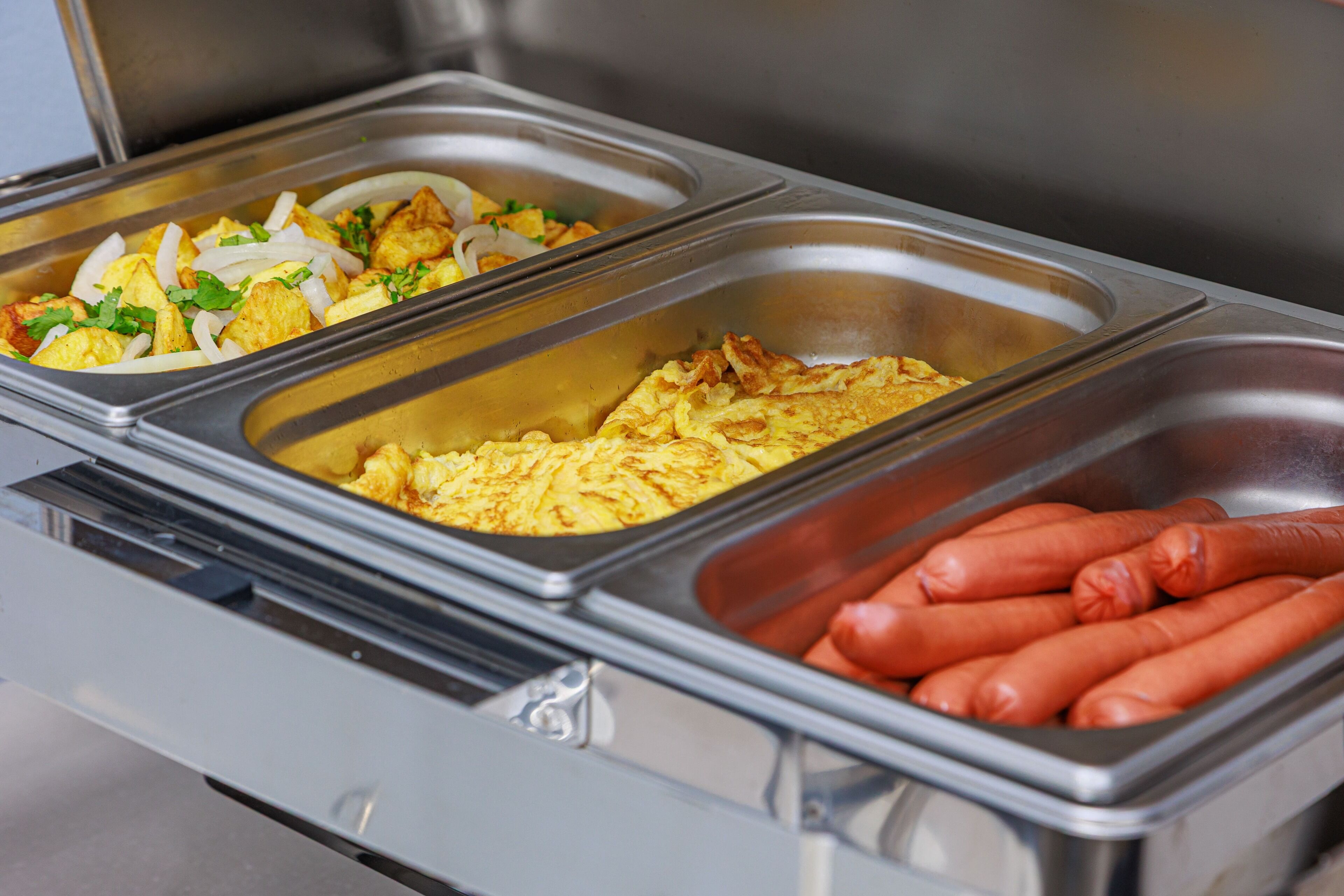 Buffet com diversas opções de comida, incluindo ovos, batatas e salsichas.
