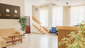 A modern hotel lobby with a sofa, a wooden reception desk, a staircase, and a potted plant. - Route Hotel (Tbilisi)