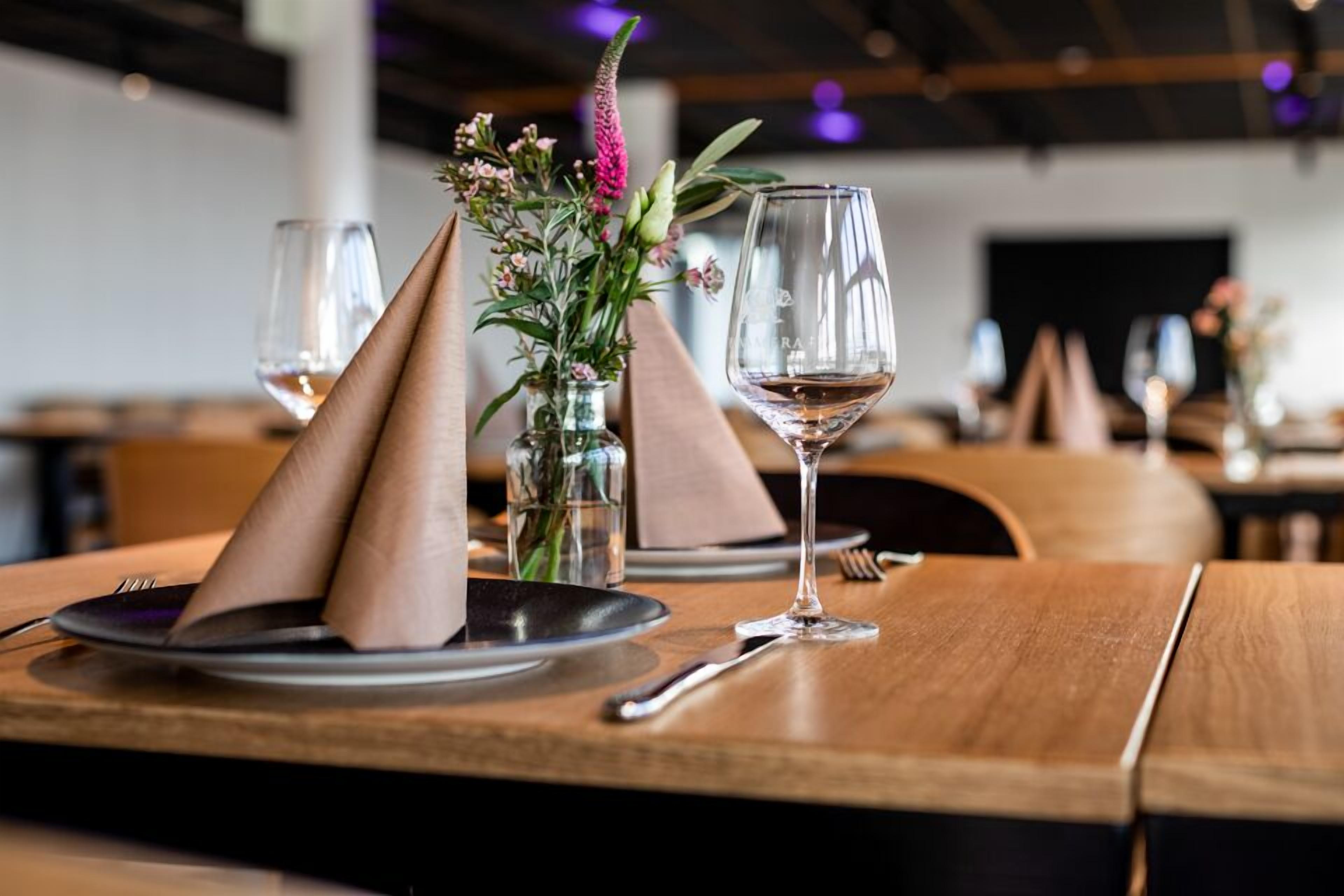 A dining table with a vase of flowers, a wine glass, and a folded napkin.